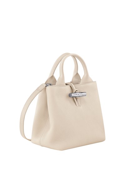 Beige leather handbag with dual top handles and an adjustable shoulder strap. Features a silver-tone hardware clasp and textured finish.
