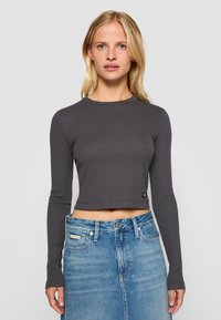 Šedý žebrovaný dlouhý rukáv crop top s kulatým výstřihem a šitým lemem. V kombinaci s denimovou sukní světle modré barvy s vysokým pasem.