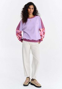 Lilla ja heleroosa pusa lillemustriliste varrukatega, kombineeritud kreemjate pükste ja pruunide matkasaabastega, millel on roosad paelad ja mustad tallad.