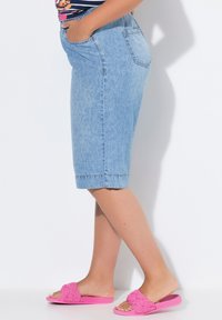Denim bermuda-shortsit vaaleansinisinä suoran mallisina, viimeisteltyinä käännetyllä helman. Yhdistettyinä vaaleanpunaisiin punottuihin sandaaleihin.