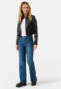 Zwarte cropped leren jas, witte T-shirt, hoogsluitende blauwe jeans en zwarte schoenen; heeft een gladde textuur en een getailleerd ontwerp.