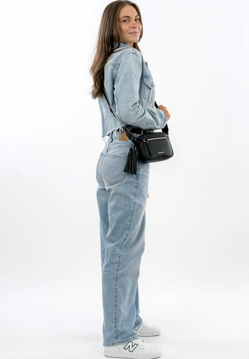 Light blue denim jacket and wide-leg jeans, paired with a small black crossbody bag featuring a tassel. White sneakers with green accents.
