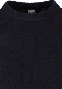 Gros plan d'un pull en maille noire avec texture à carreaux et col rond côtelé, présentant une étiquette Urban Classics à l'intérieur du col.
