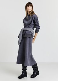 Grauer Pullover mit Kapuze, kombiniert mit einem passenden langen Rock. Das Outfit verfügt über einen gerippten Saum und wird durch schwarze Stiefeletten ergänzt.