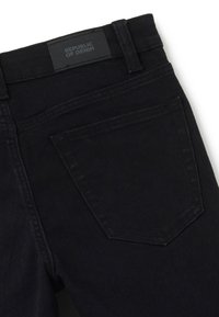 Jeans de mezclilla negros con una cintura estándar, que presentan un bolsillo trasero rectangular y una etiqueta de cuero negra embellecida con "REPÚBLICA DE MEZCLILLA."