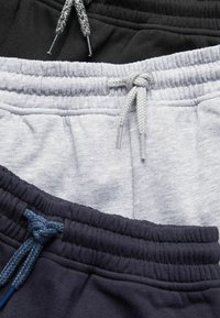 Trois paires de pantalons de survêtement en noir, gris et bleu marine. Chacune a une taille élastique avec des cordons de serrage contrastants pour un ajustement réglable.