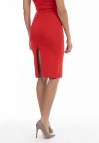 Roter, figurbetonter Strickrock mit einem Schlitz am hinteren Saum, kombiniert mit beigen High Heels, die eine glatte Textur und ein maßgeschneidertes Design zeigen.