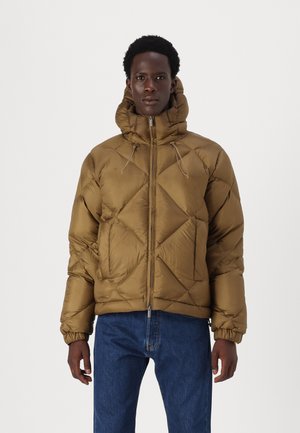 Bruine pufferjack met een strakke capuchon, diagonale quiltstructuur, ritsluiting en elastische manchetten, gedragen met blauwe jeans.