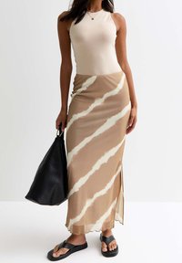 Top sin mangas beige combinado con una falda maxi larga y fluida de color marrón claro con un patrón abstracto en crema. Bolsa tote grande negra y sandalias negras.