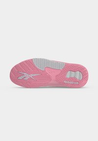 Ροζ και γκρι σόλα παπουτσιού Reebok με υφασμένους χαρακτήρες πρόσφυσης, λογότυπο Reebok κοντά στη φτέρνα και διακριτό σχέδιο πέλματος σε λευκό φόντο.