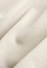 Teksturekani materijal u svijetloj bež boji s suptilnim rešetkastim uzorkom, koji prikazuje nježnu, tkanu površinu i blagi sjaj od nabora.