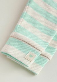 Tissu rayé avec des couleurs alternées vert menthe et crème, présentant un revers plié et une petite étiquette avec une icône de cœur.