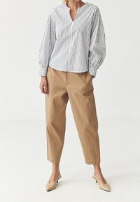 Raidallinen valkoinen ja musta paita, jossa on V-pääntie ja puffihihat, yhdistettynä beigeihin lyhyisiin housuihin ja beigeihin liukupohjaisiin korkokenkiin.