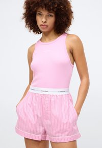 Ροζ ριγέ αμάνικο μπλουζάκι με λογότυπο Calvin Klein, συνδυασμένο με ροζ σορτς με ρίγες και ελαστική μέση με λευκές λεπτομέρειες.