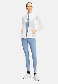 Lichte witte zip-up jas met meshpanelen, gecombineerd met aansluitende lichtblauwe leggings met verticale strepen en witte accenten.
