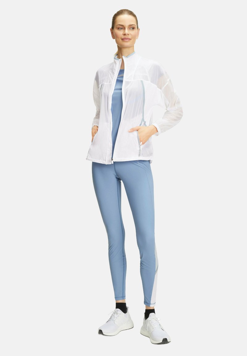 Veste blanche légère à fermeture éclair avec des panneaux en maille, associée à des leggings ajustés bleu clair avec des rayures verticales et des accents blancs.