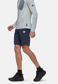 Ljusgrå långärmad tröja med en marinblå bröstficka, tillsammans med marinblå shorts med en logotyp och sidofickor, bärs med svarta träningsskor.