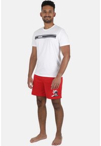 Hvid kortærmet t-shirt med sort stribe og logo, parret med røde svømmetoppe med palme grafik og logo på siden.
