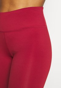 Legginsy o wysokim stanie w jednolitym burgundowym kolorze, wykonane z elastycznego materiału o gładkiej fakturze i płaskimi szwami dla komfortu i trwałości.
