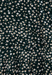 Le tissu de robe florale présente un fond vert foncé avec de petites fleurs blanches et orange, créant un motif éparpillé avec une apparence texturée.