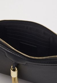 Musta nahkainen clutch-käsilaukku, jossa kultainen vetoketju. Sisäpuolella musta kangasvuori ja korttipaikkoja. Kultainen tupsu vetoketjun vetimessä.