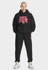 Czarna bluza z kapturem z napisem "PROSITO ATHLETIC" w wyrazistym czerwonym kolorze, w zestawie z dopasowanymi czarnymi spodniami dresowymi. Posiada luźny krój i sznurek w kapturze.