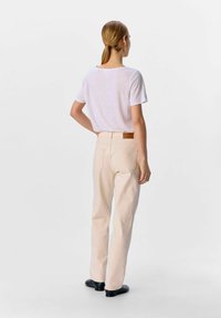 Farkut korkeavyötäröisten vaaleanbeigejen farkkujen kanssa, joissa on takataskut ja ruskea nahkainen tagi.