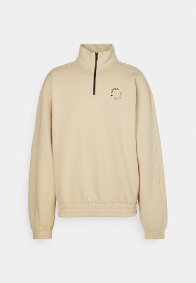 Felpa beige con zip a quarto, realizzata in tessuto morbido, con orlo a coste, polsini elastici e un logo circolare sul petto.