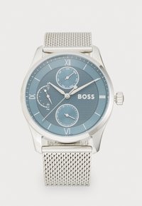 Reloj de malla plateada con una esfera redonda azul, números romanos, tres subesferas y una superficie texturizada. Nombre de la marca "BOSS" mostrado de forma prominente.