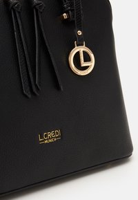 Sac à main en cuir noir avec pompons, ferrures dorées et logo L. Credi. Texture lisse et forme structurée, avec un design élégant.