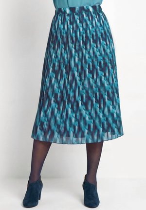 Blau und schwarz gemusterter plissierter Midirock, getragen mit durchscheinenden schwarzen Strumpfhosen und dunkelblauen Wildleder-Stiefeletten.