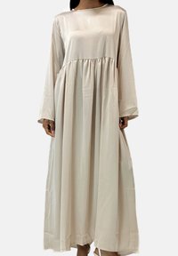 Lang, flydende kjole i et lyst beige satinmateriale med rund halsudskæring, lange ærmer og en indsnævret talje med to sidelommer.