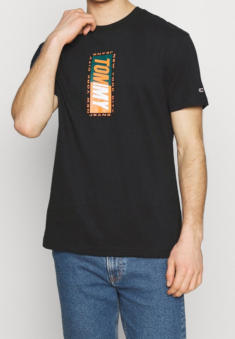 Czarny bawełniany T-shirt z krótkimi rękawami, z pomarańczowym i zielonym prostokątem z logo, na którym napisano "TOMMY NEW YORK CITY JEANS."