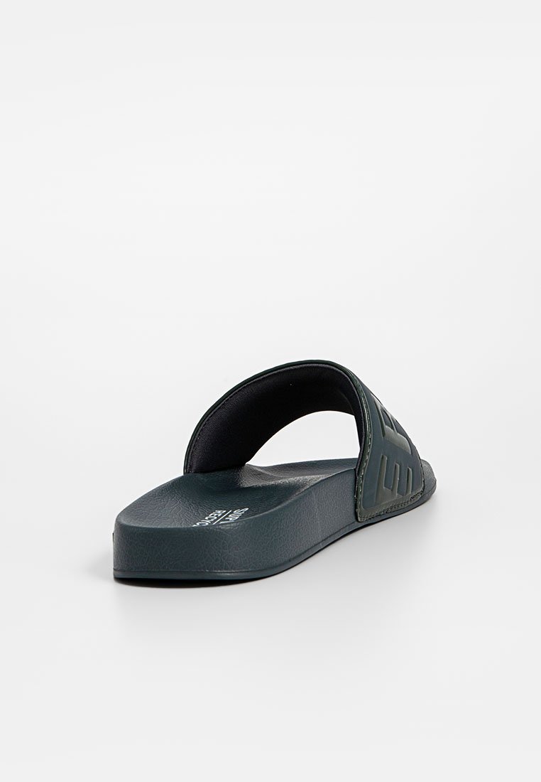 Sandale glissante verte avec un upper en caoutchouc texturé et une semelle plate. Dispose d'un bout ouvert et d'une large sangle sur le pied.