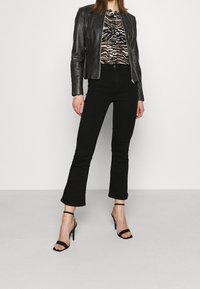 Černá kožená bunda, vzorovaný top, černé rozšířené džíny a černé sandály na podpatku. Hladké materiály a přiléhavý střih.