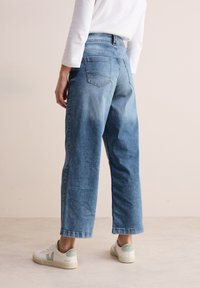 Vaaleansinisen denim-kangasta olevat leveälahkeiset farkut, joissa on korkea vyötärö, kahdet takataskut ja hieman haalistunut pinta. Yhdistettynä valkoisiin lenkkareihin.