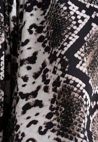 Tessuto in bianco e nero caratterizzato da un motivo a pelle di serpente con diverse texture, forme e tonalità di beige e crema per creare contrasto.