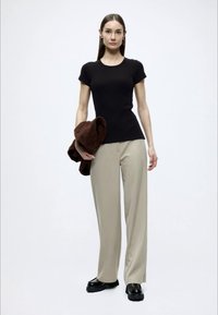 Μαύρο τοπ με κοντά μανίκια, μπεζ παντελόνια με φαρδιά μπατζάκια και μαύρα χοντρά παπούτσια. Ένα καφέ σακάκι είναι περασμένο σε ένα χέρι.