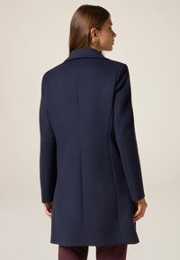 Cappotto in lana navy con design sartoriale, colletto a stecco e maniche lunghe. Presenta una linea dritta e una texture liscia.