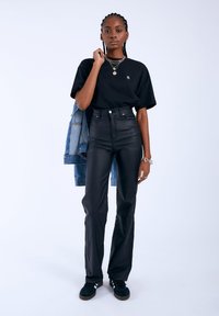 Svarta högmidjade läderbyxor i kombination med en svart t-shirt och en denimjacka. Outfiten pryds av lager av halsband och svarta sneakers.