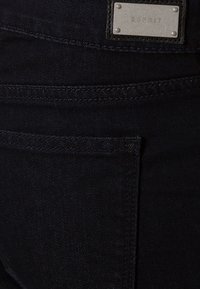 Tissu en jean bleu foncé avec une poche arrière et une étiquette métallique de la marque Esprit cousue au-dessus de la poche.
