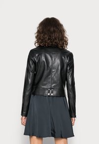 Svart läderjacka med figursydd design, som har en slät yta, dragkedjor vid ärmsluten och en dubbeknappad detalj baktill.