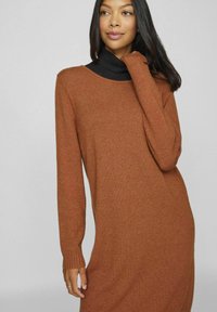 Abito a maniche lunghe color ruggine con una morbida texture in maglia e una vestibilità rilassata. Presenta polsini a coste e una ampia scollatura a barchetta.