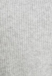 Tissu tricoté gris clair avec une texture côtelée, présentant des variations subtiles de nuances. Le matériau semble doux et chaud.