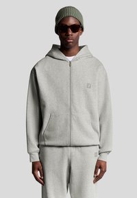 Grå zip-up hoodie lavet af blød stof har en kengurulomme, ribbede ærmer og et broderet logo på brystet. Matchet med matchende bukser.