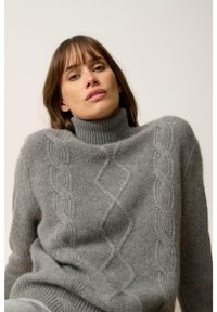Szary sweter z wysokim ryżowym kołnierzem, z teksturowanymi wzorami w warkocz z przodu. Miękka, dziana tkanina o luźnym kroju.