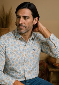 Bloemenprint shirt met een lichtblauwe achtergrond, voorzien van beige bloemen en blauwe accenten. Je kunt het sluiten met knopen en het heeft lange mouwen met knoopmanchetten.