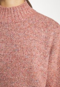 Pull en tricot rose avec un col montant côtelé. La texture est épaisse et confortable, avec des touches de couleurs vives dans tout le tissu.