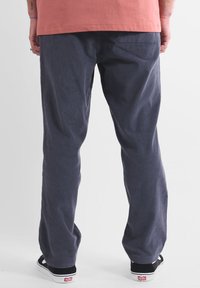 Pantalon en velours côtelé bleu marine avec une coupe droite. Comprend une poche arrière et des baskets noires. Accompagné d'une chemise de couleur claire.