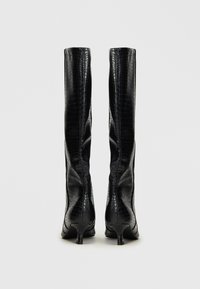 Botas negras hasta la rodilla hechas de cuero con relieve de cocodrilo, con un eje ajustado, punta afilada y un tacón bajo tipo kitten.